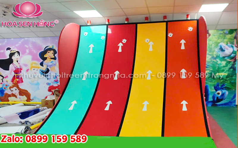 Hình ảnh trẻ em hào hứng leo dốc bấm chuông trong khu vui chơi, với bề mặt leo đầy màu sắc và chuông chiến thắng ở đỉnh cao