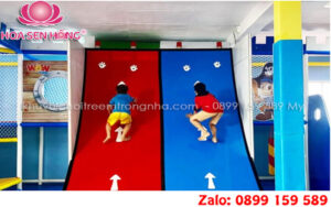 Hình ảnh trẻ em hào hứng leo dốc bấm chuông trong khu vui chơi, với bề mặt leo đầy màu sắc và chuông chiến thắng ở đỉnh cao